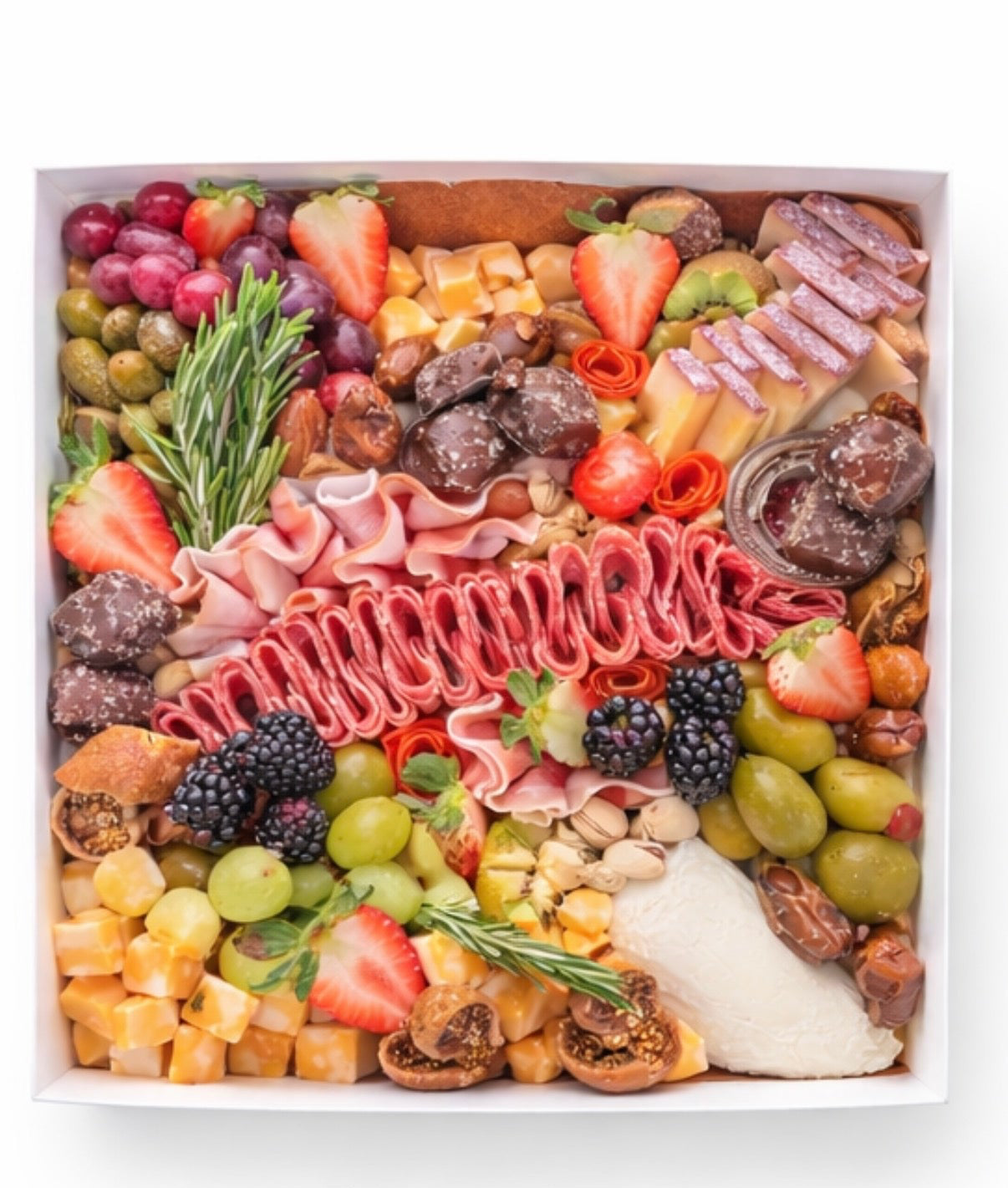 Assorted charcuterie food items including fruits, meats, and cheeses arranged in a box. 